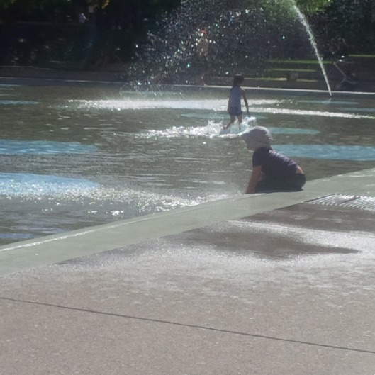 A girl plays with the water at Olympic Plaza across from City Hall, Calgary Alberta